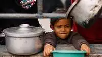 Ein kleines Kind hält eine Schüssel mit ausgestreckten Armen und wartet auf die Verteilung von Essen
